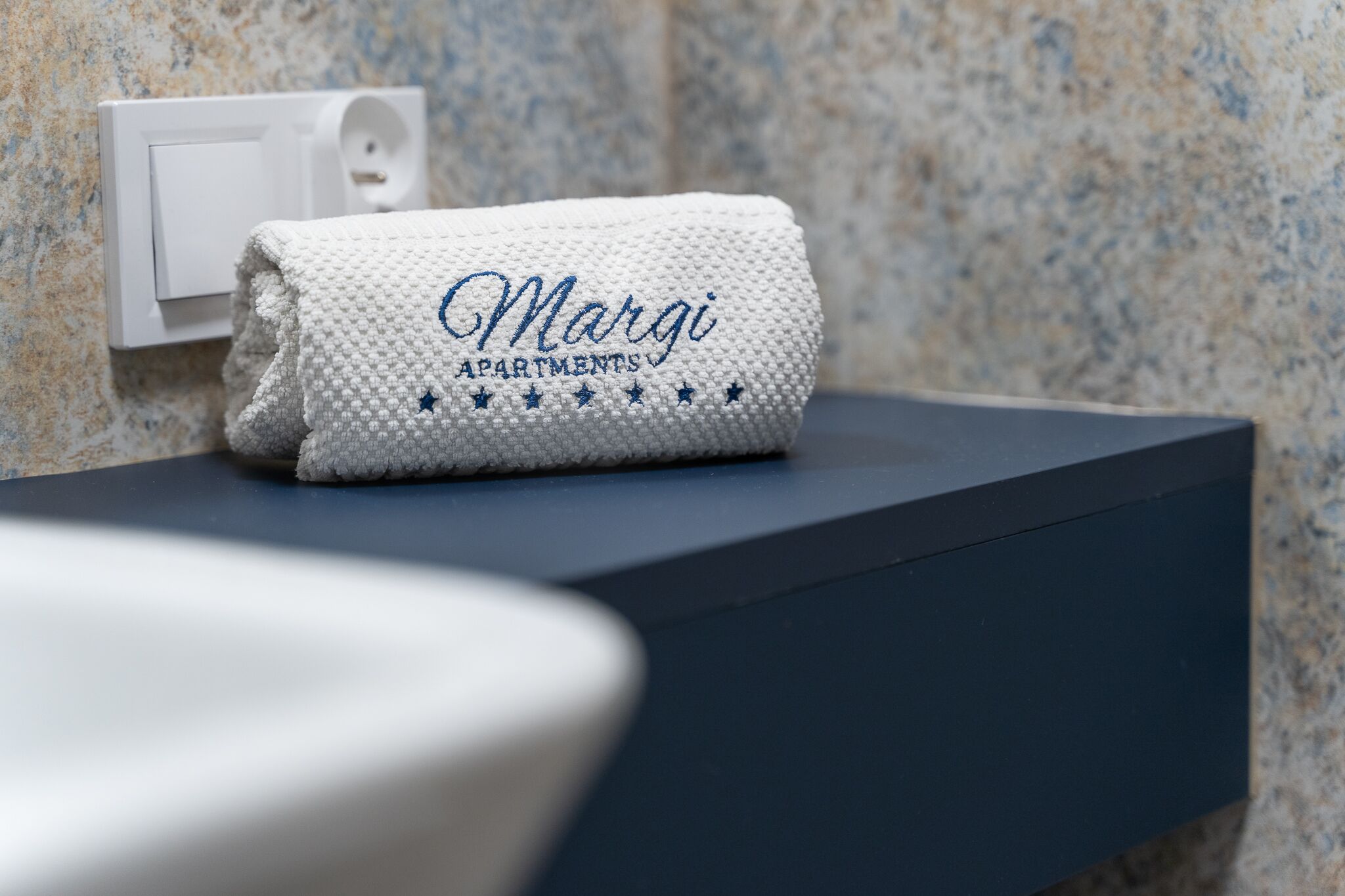 A folded towel with embroidered text on a dark countertop against a textured wall.