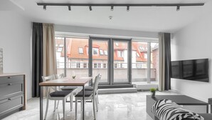 A modern living room with a dining area, large windows, and a TV mounted on the wall. - MARGI Gran Apartament (Szczecin)