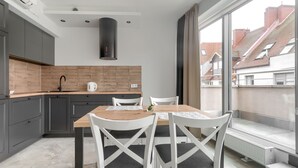 A modern kitchen with grey cabinets, a brick backsplash, and a large window overlooking a residential area. - MARGI Gran Apartament (Szczecin)