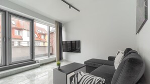 A modern living room with a sofa, a coffee table, and a TV mounted on the wall. - MARGI Gran Apartament (Szczecin)