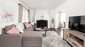 A modern living room with a sofa, a fireplace, a television, and a large window. - Backyard+Porch, Pet-Friendly | Broad Ripple Stay (Indianapolis)