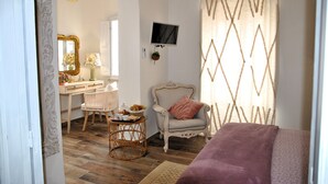 Une pièce avec un plancher en bois, un lit, une chaise, un bureau avec une lampe, un téléviseur et un rideau à motifs.
