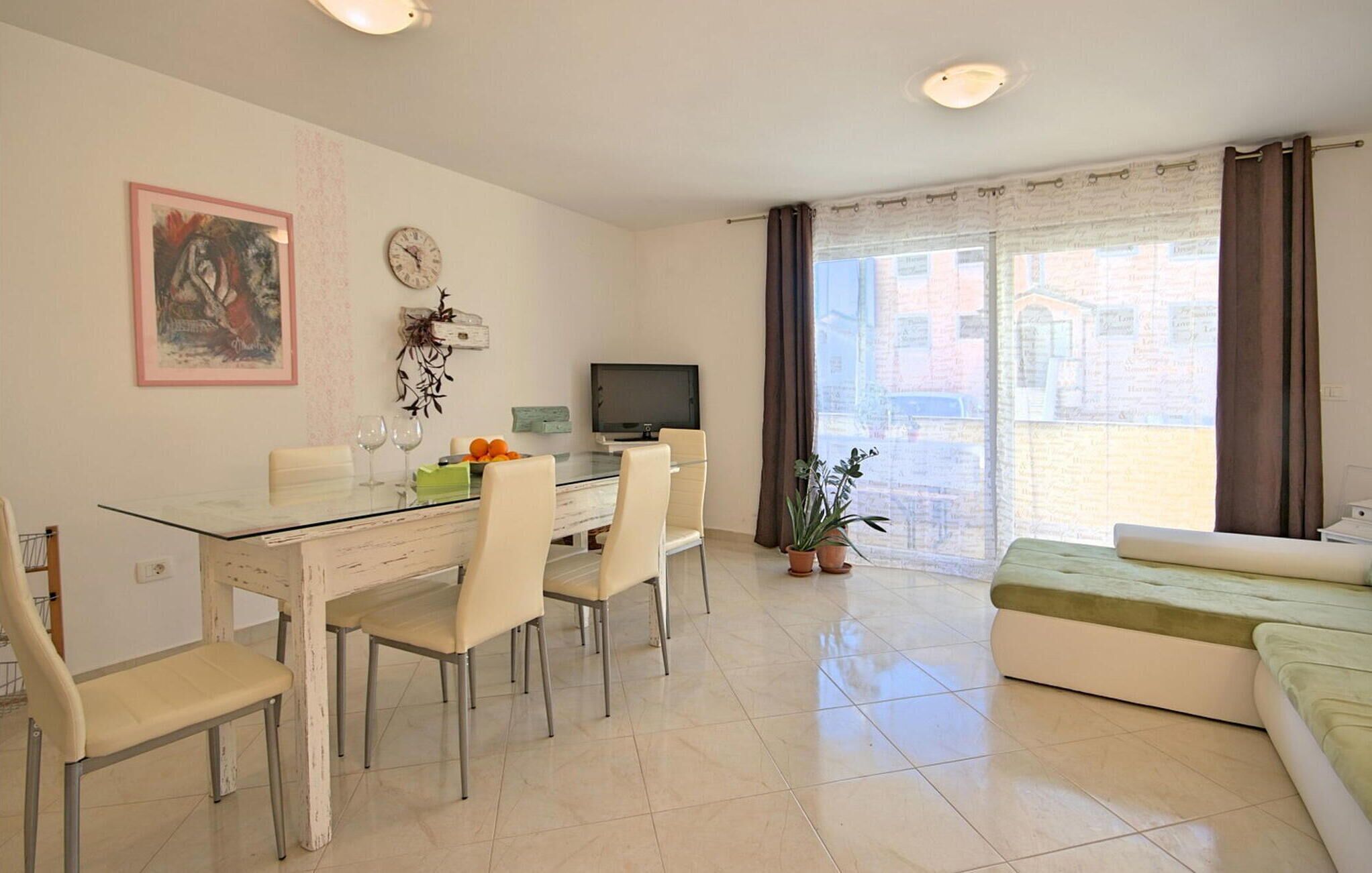 A modern living room with a dining area, a flat-screen TV, a sofa, and a potted plant.