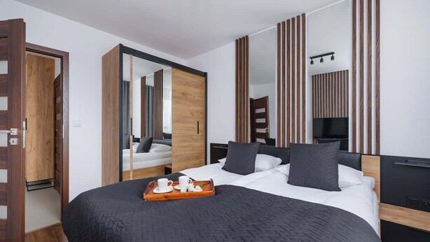 A modern hotel room with a large bed, a wooden wardrobe, a mirror, and a TV.