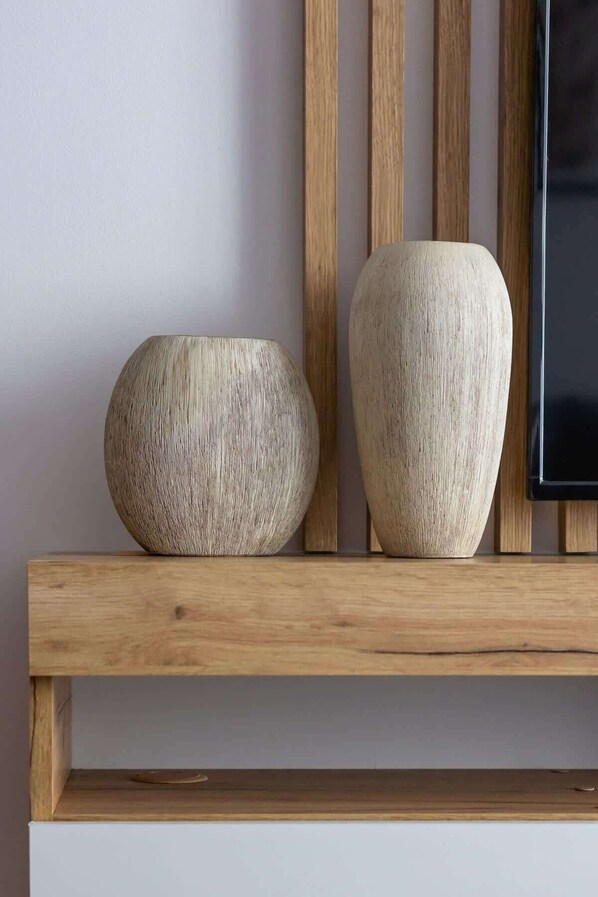 Dos jarrones de madera sobre una estantería frente a una pared con listones de madera verticales.
