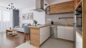 A modern kitchen with wooden cabinets, a built-in dishwasher, and a dining area with a gray sofa and a small wooden table.