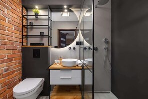 Un baño moderno con pared de ladrillo, tocador de madera, inodoro blanco y cabina de ducha de vidrio.