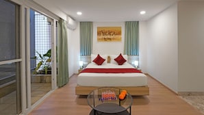 A modern hotel room with a large bed, a glass coffee table with chess pieces and oranges, and a view of a balcony with plants. - Nest By Rivido Apart Hotel (Bengaluru)