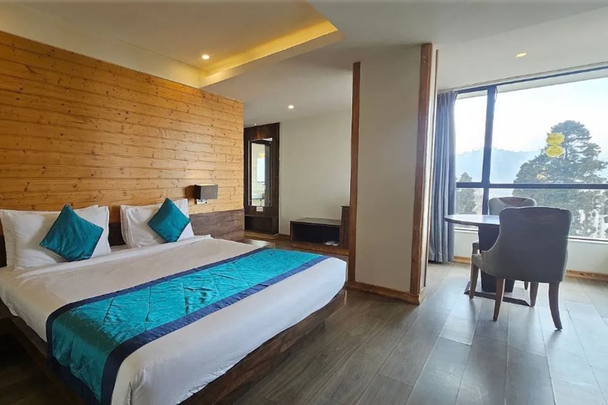 Habitación de hotel moderna con una cama grande, cabecera de madera, un escritorio y un ventanal con vistas.