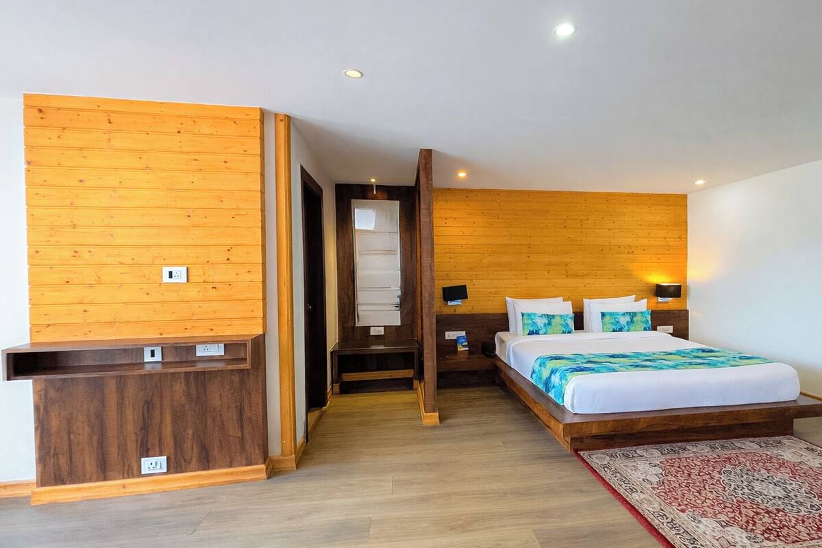 Una habitación de hotel moderna con una pared de acento de madera, una cama con colcha azul y blanca, una mesita de noche y un pequeño escritorio con silla.