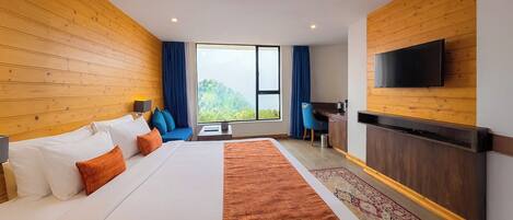 Habitación de hotel con una cama grande, un escritorio, un televisor y vistas a zonas verdes.