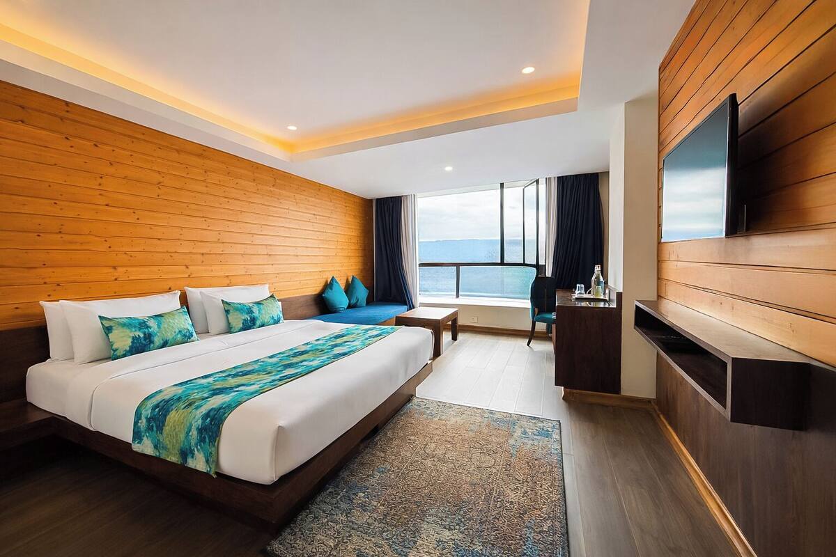 Habitación de hotel moderna con una cama grande, paneles de madera, televisión y vista al mar.