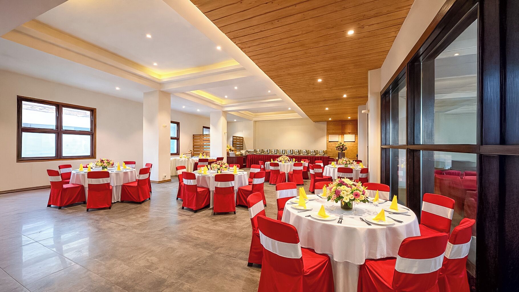 Un salón de banquetes con mesas redondas, sillas rojas y blancas, y techo de madera.