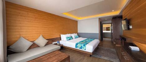 A modern hotel room with a wooden wall, a large bed with a blue and white blanket, a wooden bench, and a TV mounted on the wall.