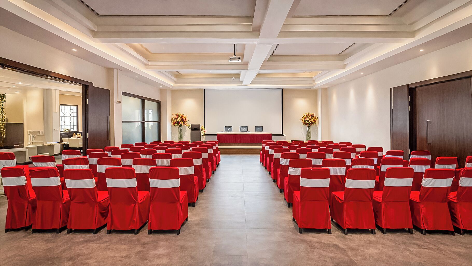 A conference room with rows of chairs, a stage, and a projector screen.