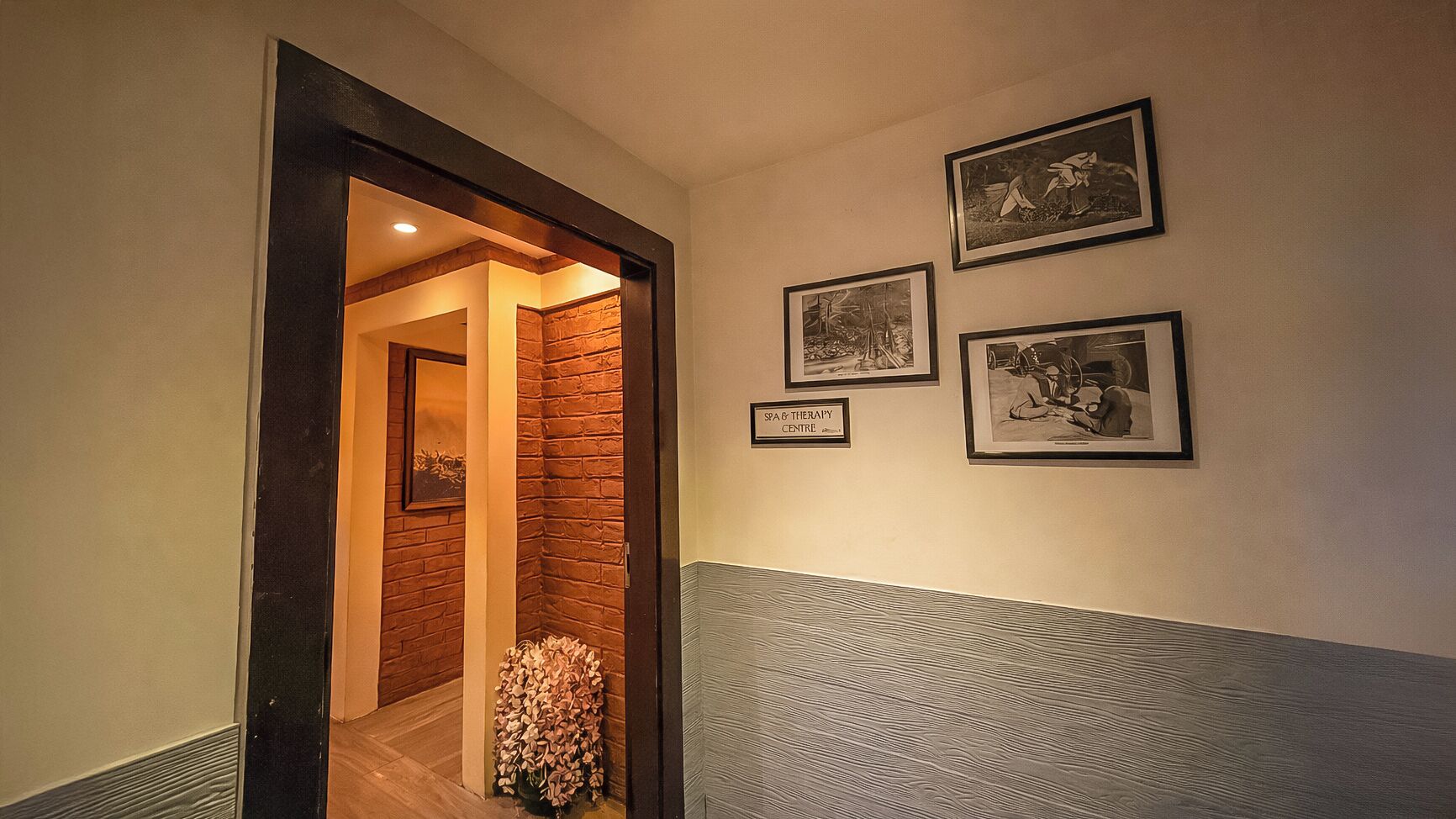 A hallway with a wooden floor, a brick wall, and framed pictures on the wall.