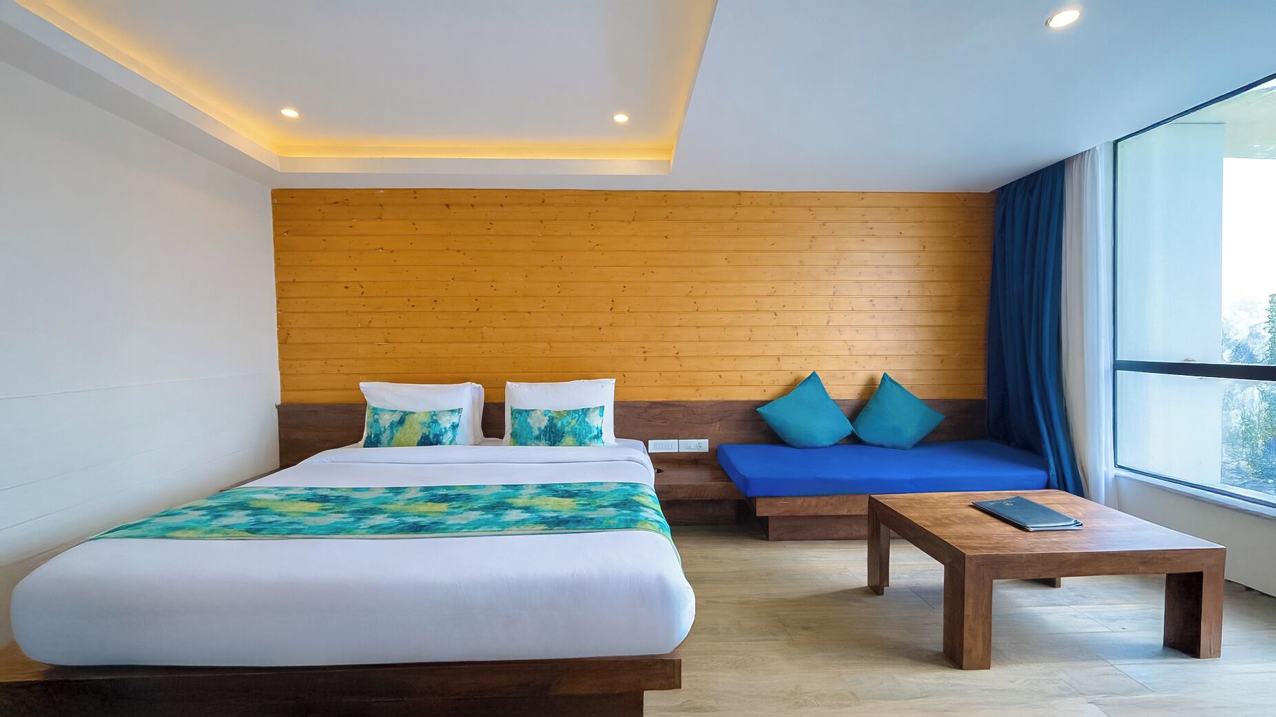 A hotel room with a bed, a sofa, a coffee table, and a large window.