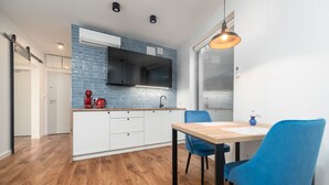 A modern kitchen with a wooden countertop, white cabinets, and a blue backsplash. There is a dining area with a wooden table and blue chairs. - MARGI Figo Apartament (Szczecin)