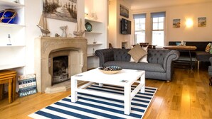 A living room with a fireplace, a grey sofa, a white coffee table, and a striped rug. - Beach in Reach - group house for up to 14 with sea views (Eastbourne)