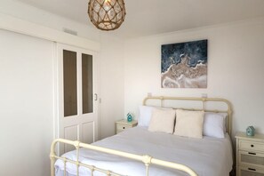 Um quarto com cama, porta, mesa de cabeceira, quadro na parede e luminária suspensa.