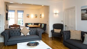 A living room with two grey sofas, a coffee table, and a dining area with a table and chairs. - Beach in Reach - group house for up to 14 with sea views (Eastbourne)