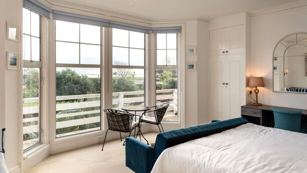 A bedroom with a large bay window, a bed, a chair, a desk, and a ceiling fan. - Beach in Reach - group house for up to 14 with sea views (Eastbourne)
