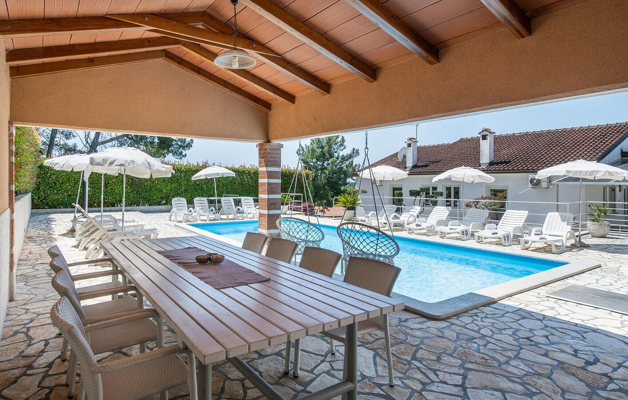 A covered outdoor area with a pool, lounge chairs, and a table.