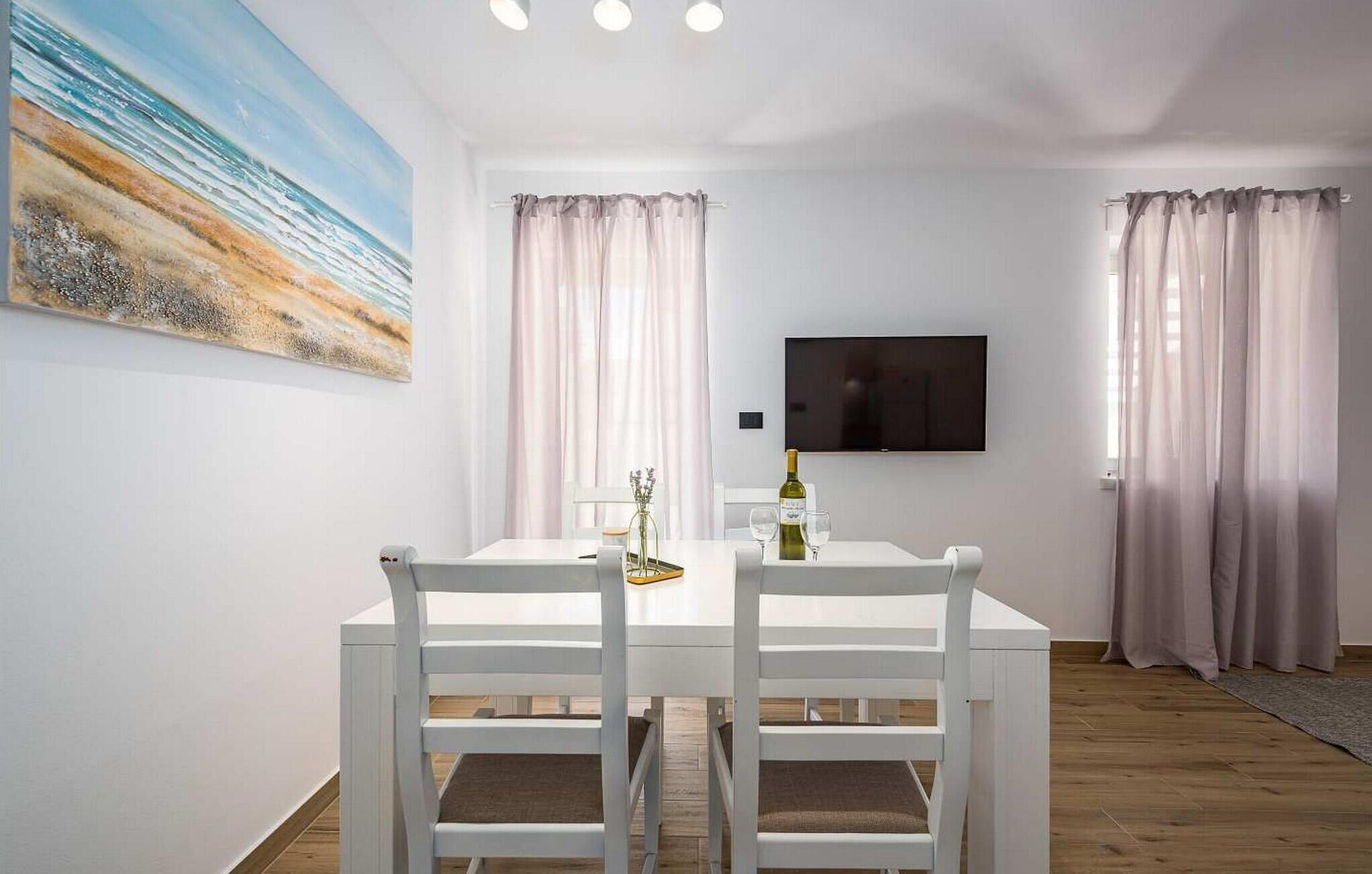 Un comedor con una mesa y sillas blancas, un cuadro en la pared y un televisor colocado encima de la mesa.