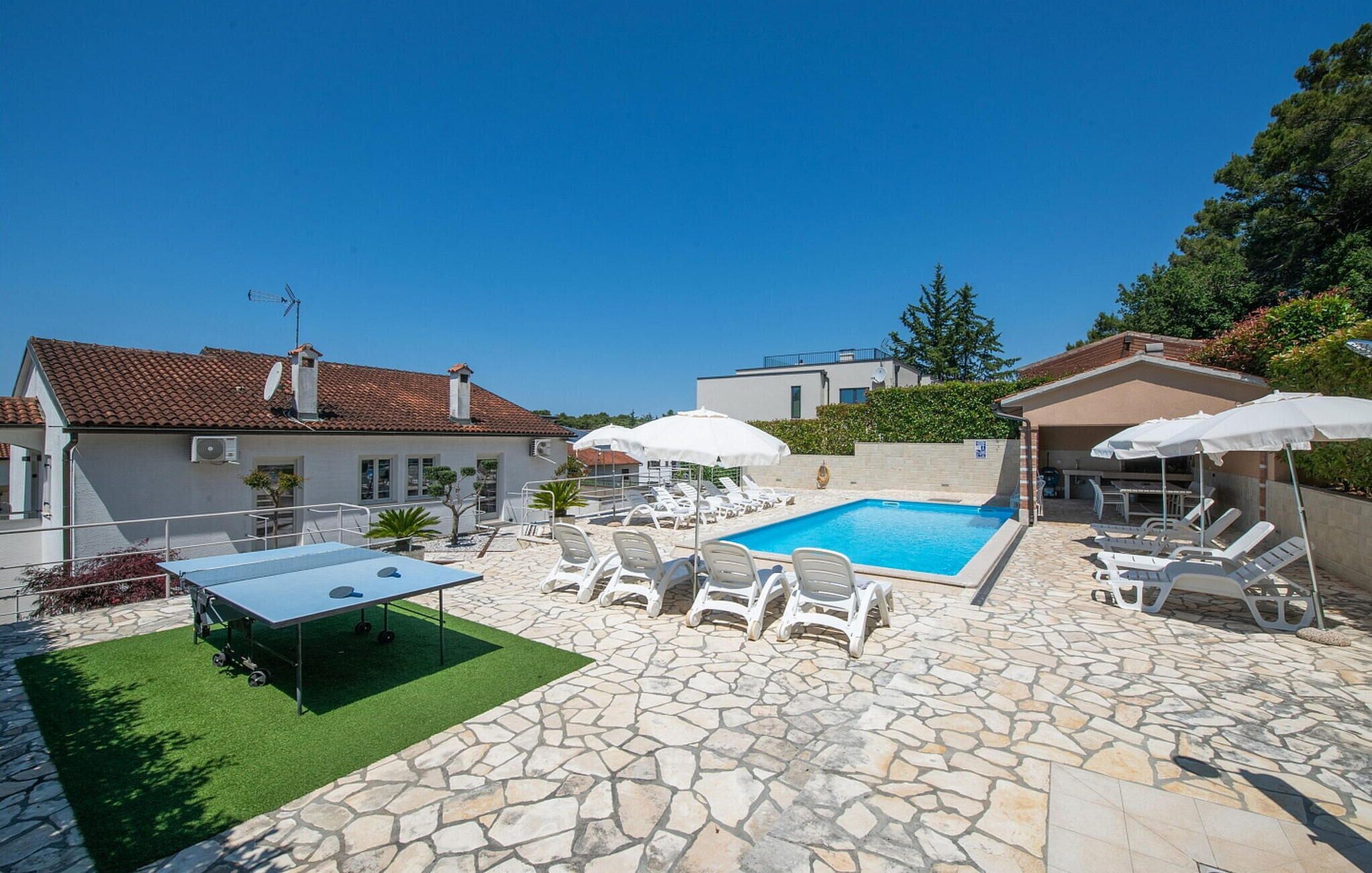 A pool area with lounge chairs and umbrellas, surrounded by stone flooring and a small table.