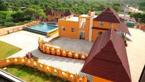 Un edificio grande con piscina, rodeado de vegetación y montañas al fondo.