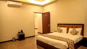 Una habitación de hotel con una cama grande, mesitas de noche, un climatizador y una puerta que da a otra habitación.