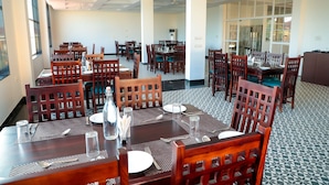 Un comedor con varias mesas y sillas, dispuesto en un espacio amplio con ventanas grandes que dejan entrar luz natural.