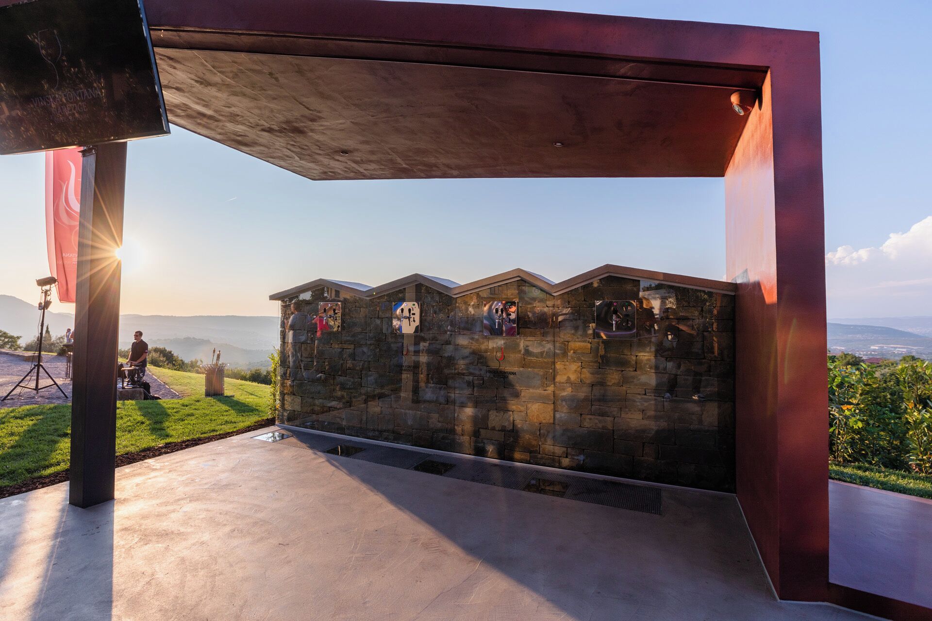 Un padiglione moderno all'aperto con un muro in pietra e un tetto in metallo, con vista panoramica sul paesaggio.