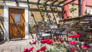 Un patio de paredes de piedra con una puerta de madera, asientos exteriores y una pérgola.
