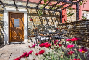 Un patio de paredes de piedra con una puerta de madera, asientos exteriores y una pérgola.