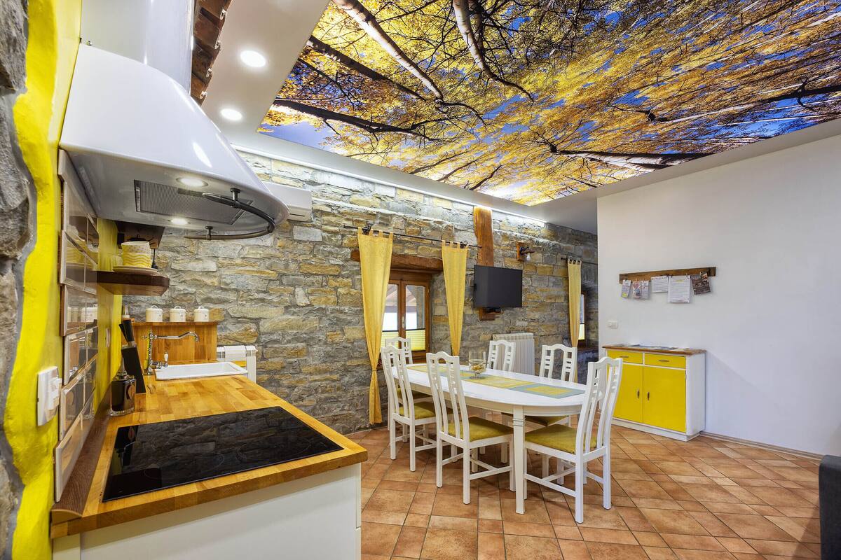 A kitchen with a stone wall, wooden counter, and a ceiling with a tree branch design.