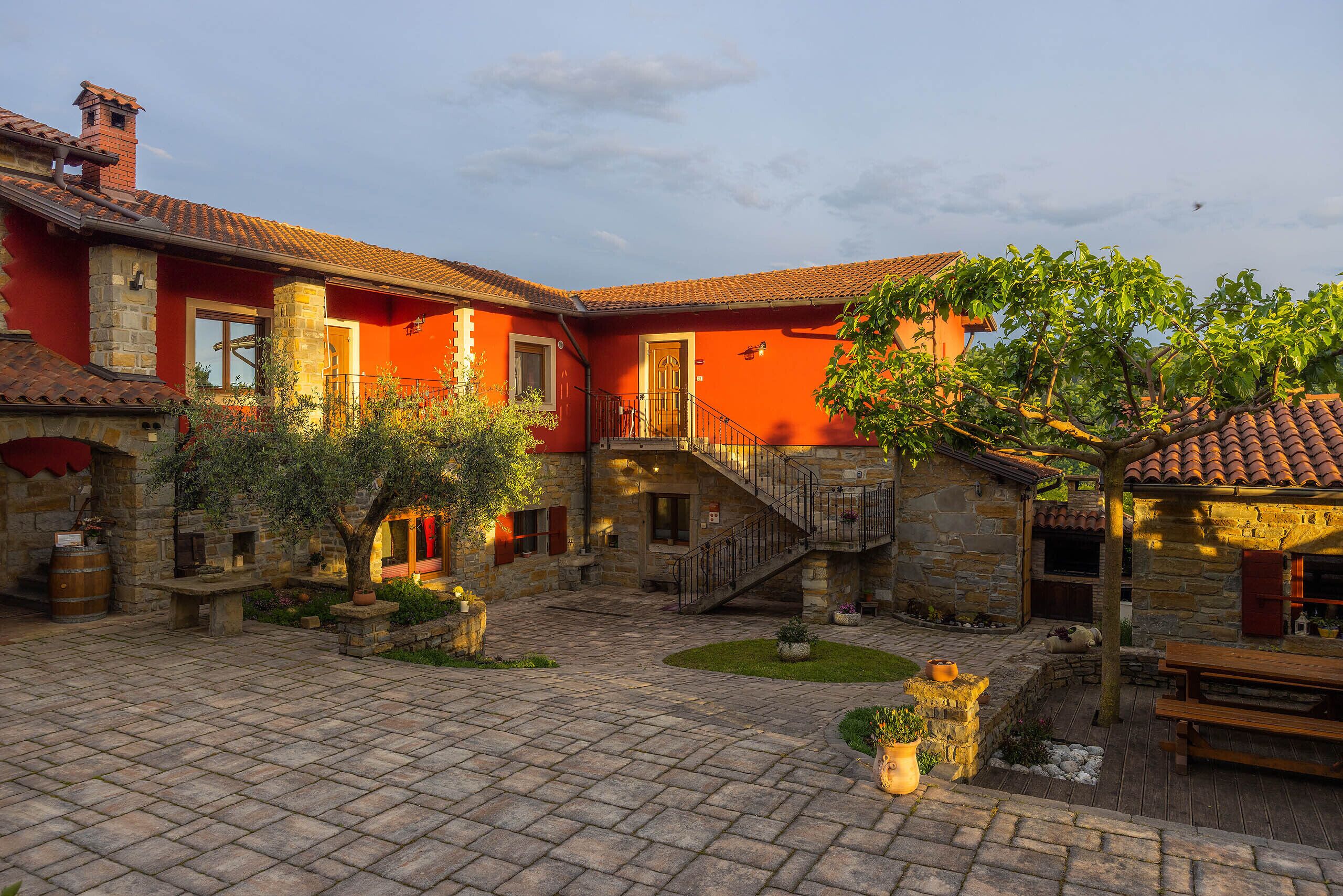 A courtyard with stone flooring, a wooden bench, and a staircase leading to a second level.