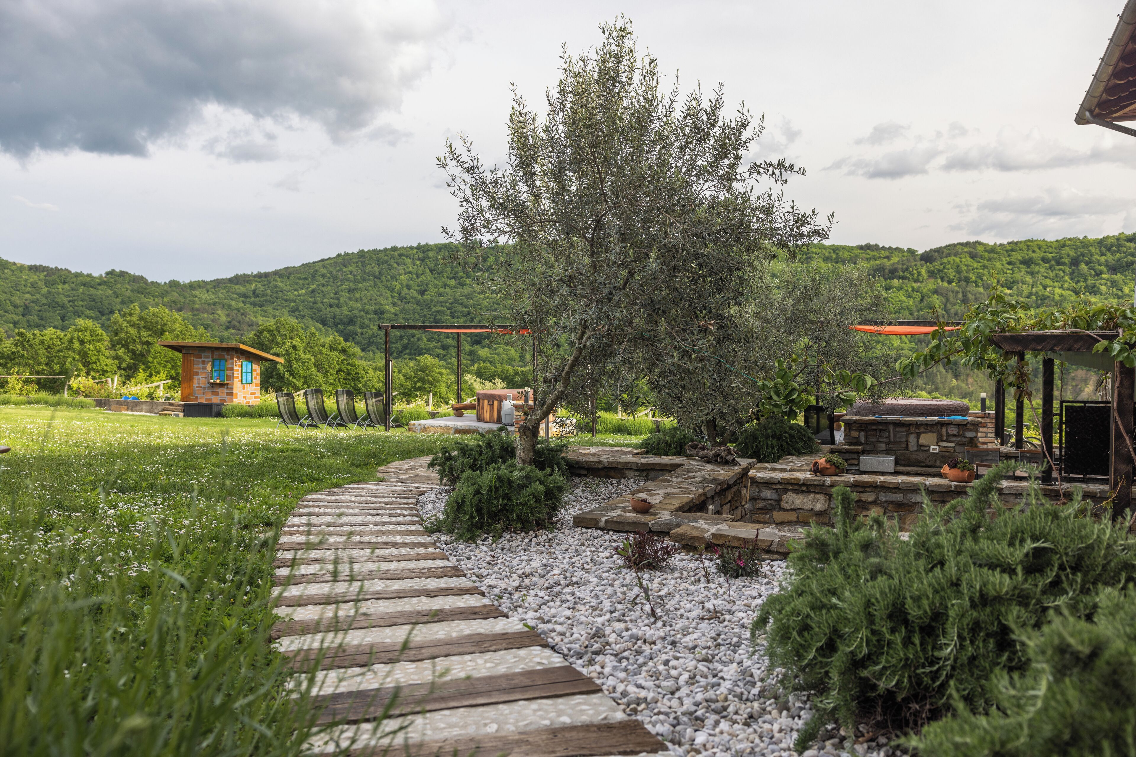 A garden pathway leading to a rustic wooden structure with a stone wall and potted plants.