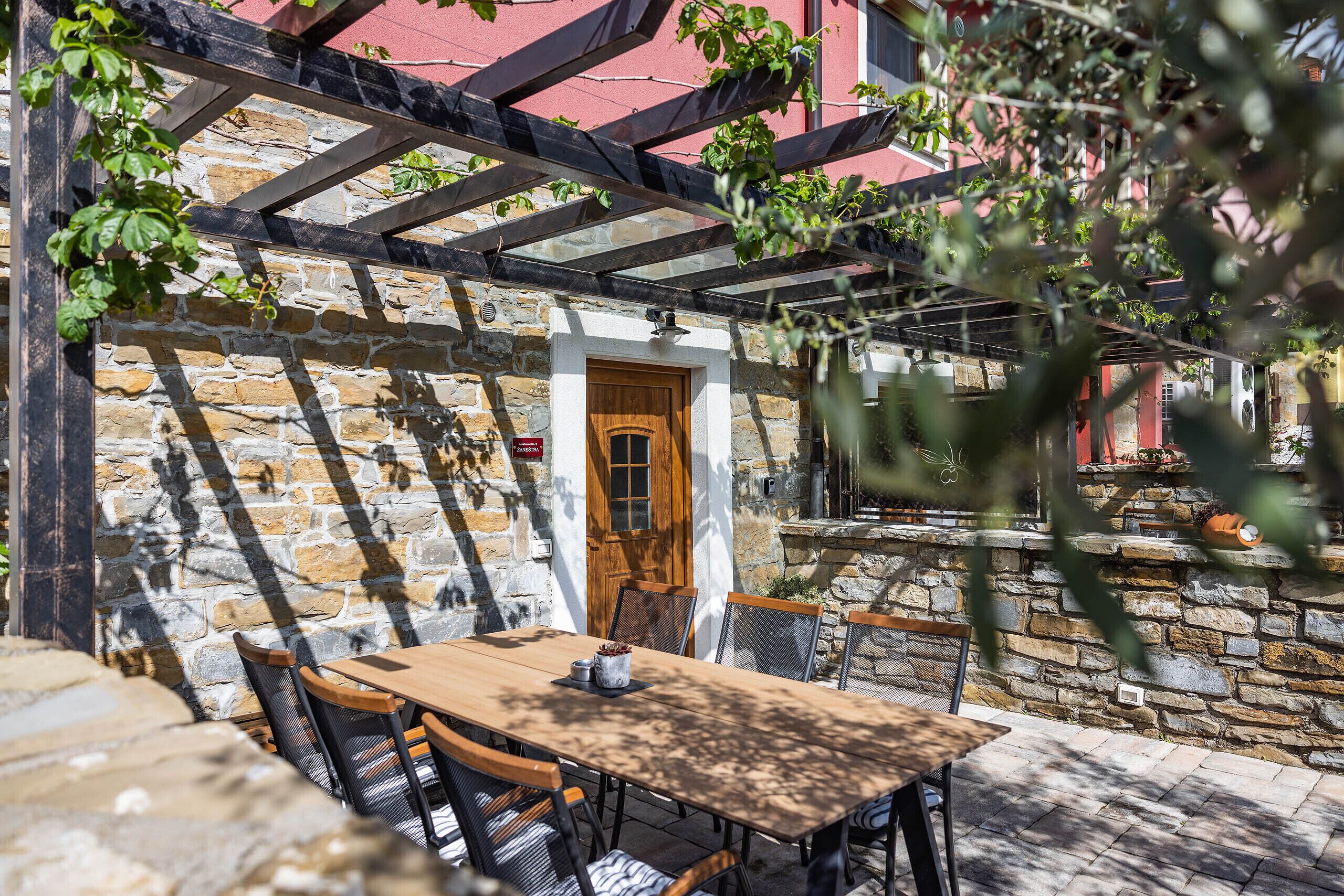 An outdoor patio with a stone wall, wooden door, and a table with chairs.