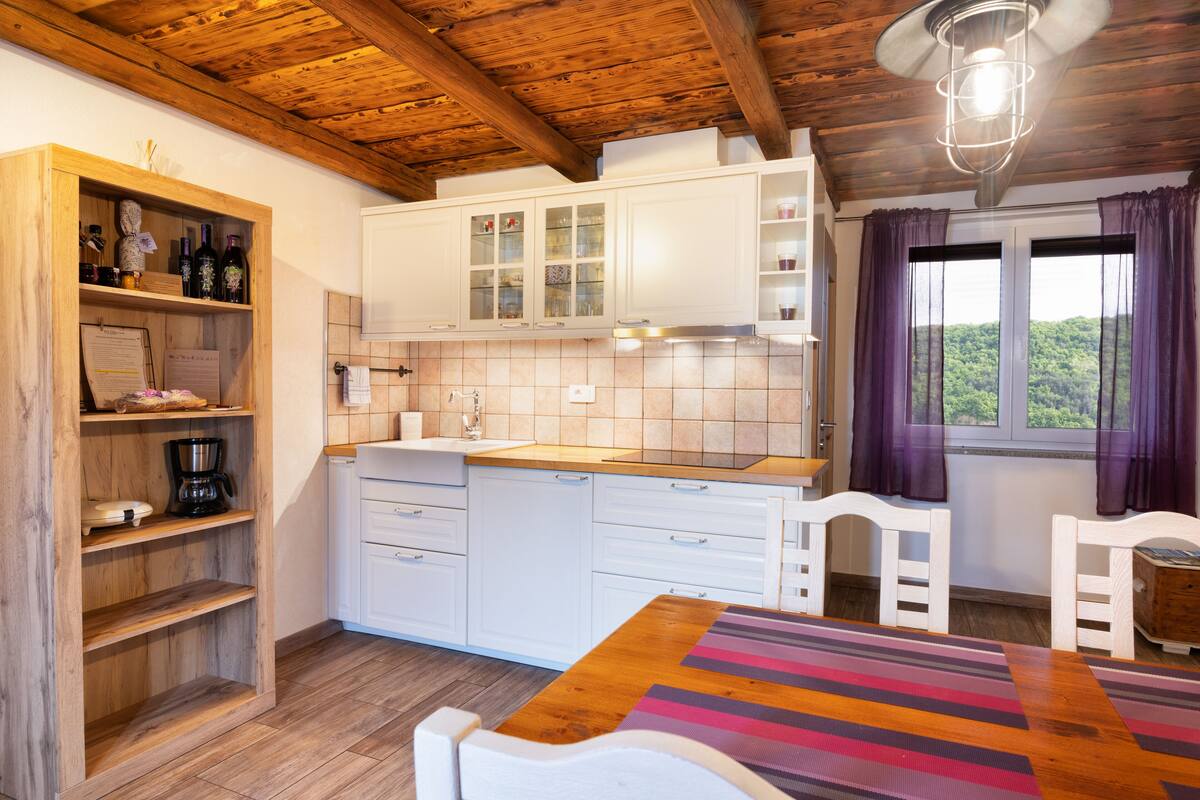A kitchen with wooden cabinets, a coffee maker, and a window with curtains.