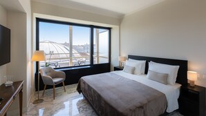Une chambre d’hôtel moderne dotée d’un grand lit, de deux tables de chevet, d’une chaise et d’une grande fenêtre donnant sur la ville.