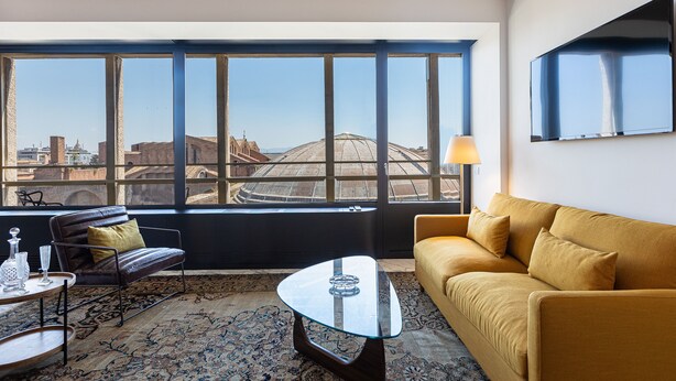 Un salon moderne avec un canapé, une table basse en verre et une vue sur le paysage urbain, visible à travers de grandes fenêtres.