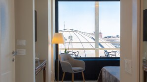 Une chambre d’hôtel avec une grande fenêtre, une chaise, une table de chevet et un lit.