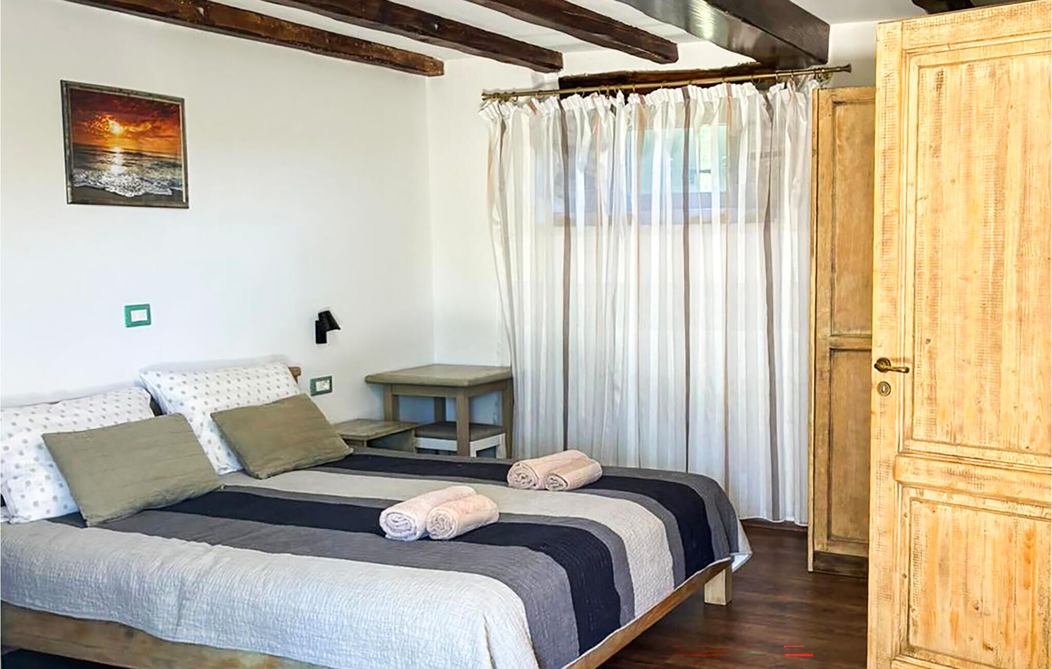 Ein Schlafzimmer mit einem Bett, Kissen, einem Nachttisch, einem Vorhang und einem Holzschrank.
