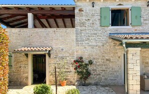Un bâtiment en pierre avec un toit en tuiles, une porte en bois et un petit jardin agrémenté de plantes en pot et de fleurs.