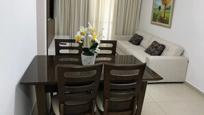 A dining area with a table and chairs, a sofa, a painting, and a TV on the wall. - Apto 2/ Q próximo ao Hospital premium (Goiania)