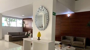 A modern lobby with a white reception desk, a large ornate mirror, and two sofas. - Apto 2/ Q próximo ao Hospital premium (Goiania)