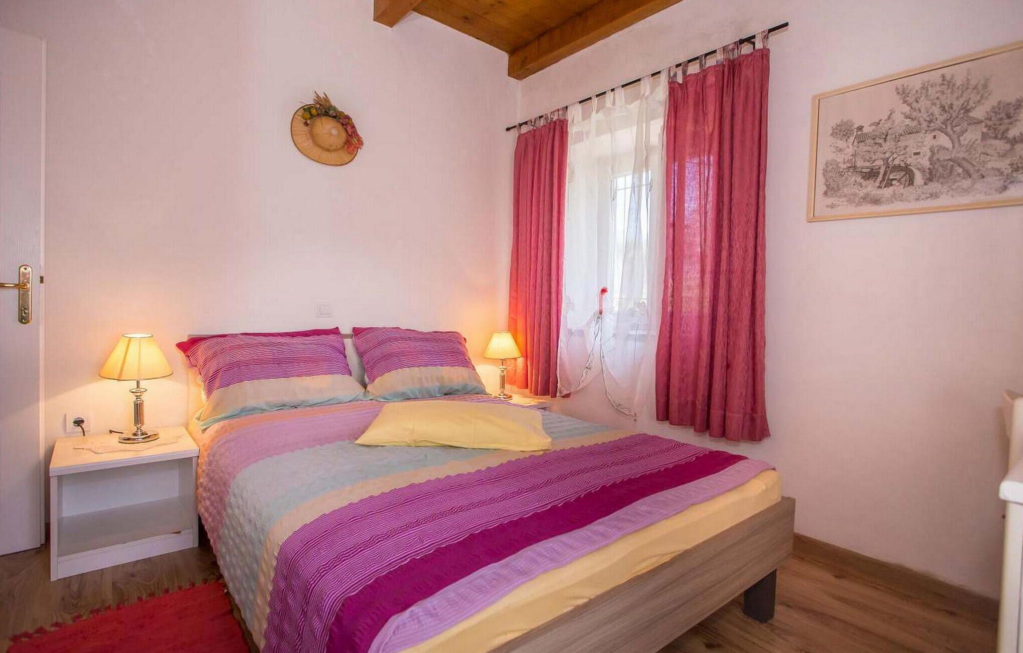 A bedroom with a bed, two bedside tables with lamps, a wooden floor, and a painting on the wall.