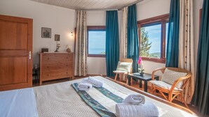 A bedroom with a bed, a wooden dresser, a chair, a small table, and a window with curtains. - DN Beach Coast Villa (Zakynthos)