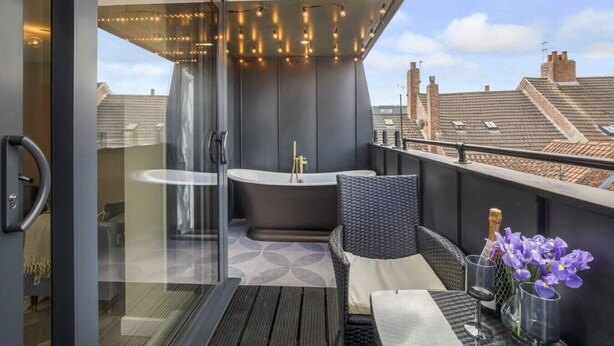 A balcony with a modern bathtub, wicker furniture, and a glass door leading to a room. - The Tree house, York (York)